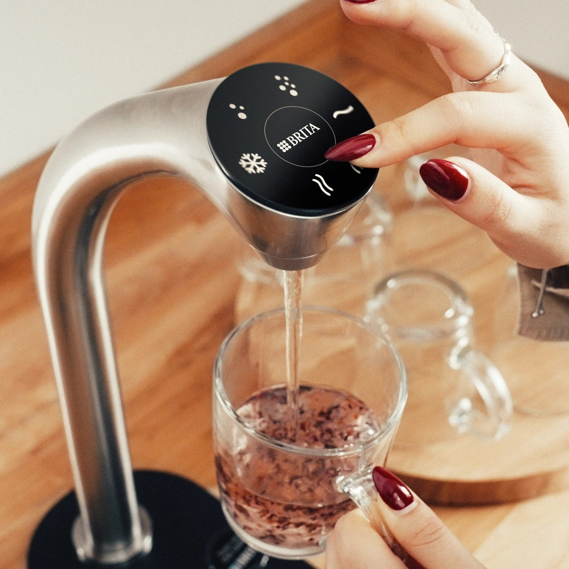 Person using a BRITA Extra C-Tap to dispense hot water into a glass with tea leaves.