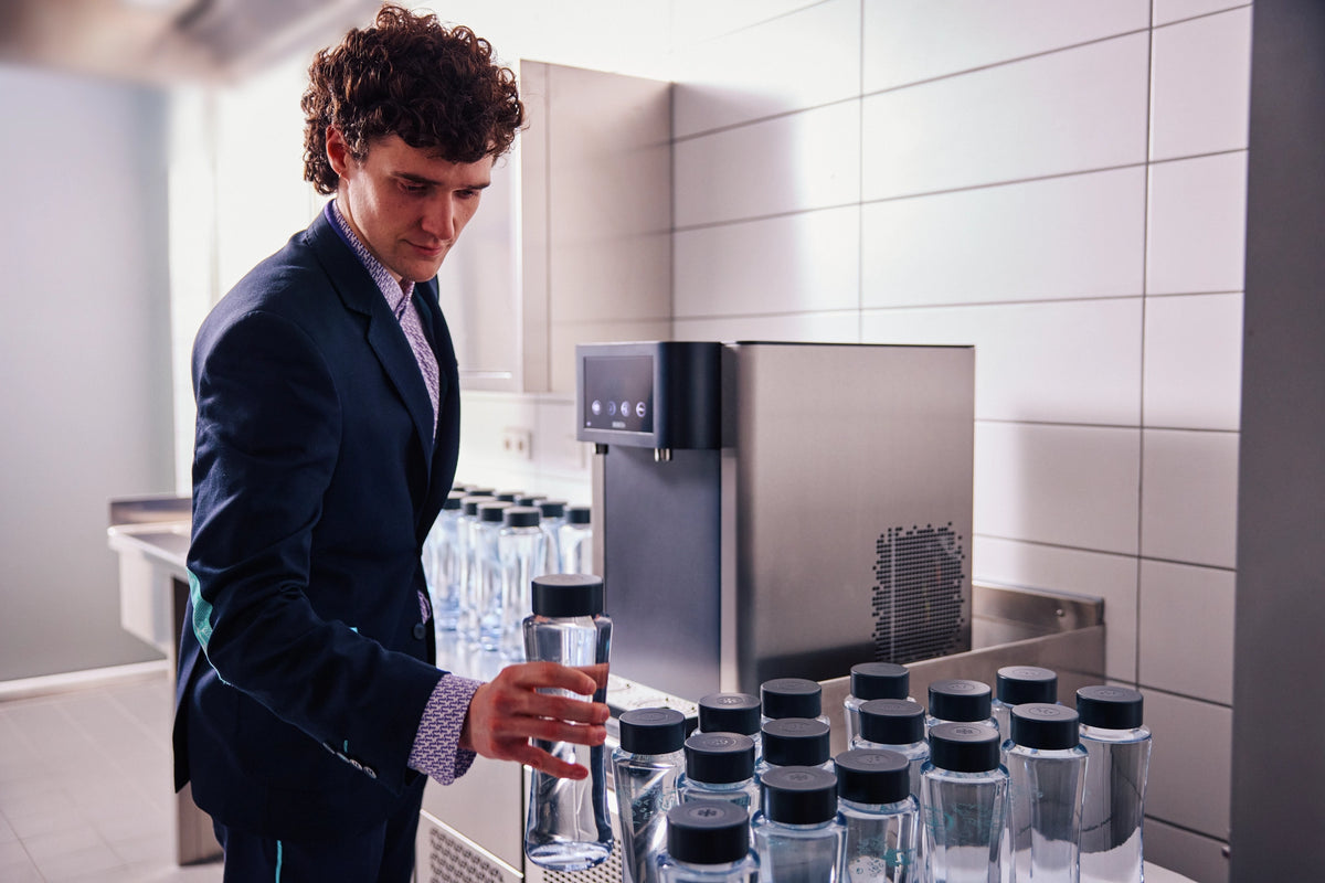 Man in a suit standing in front of a Fill Pro dispenser filling up multiple bottles.