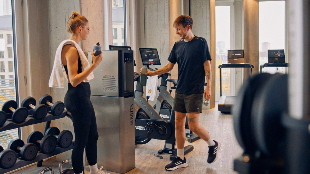 People filling their bottles at a BRITA Top Pro water dispenser in a gym.