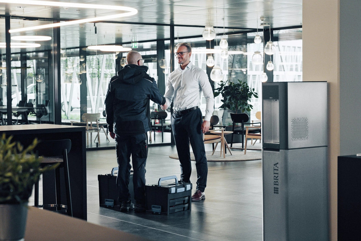 Two men shaking hands in a modern office setting with a BRITA Top Pro in the foreground.